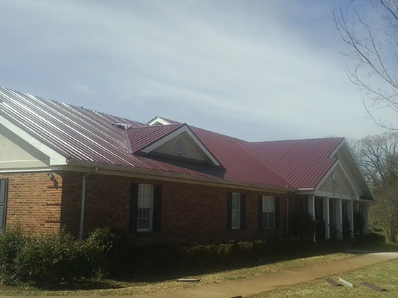 Red metal roof with gabled entries on a long brick building, from a Hail Damage Roof Repair job in Wampum
