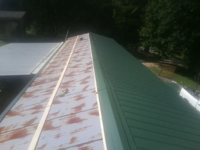 Old rusted panels beside newly installed green metal roofing — Wind Damage Roof Repair by Roofing Brothers in Wampum