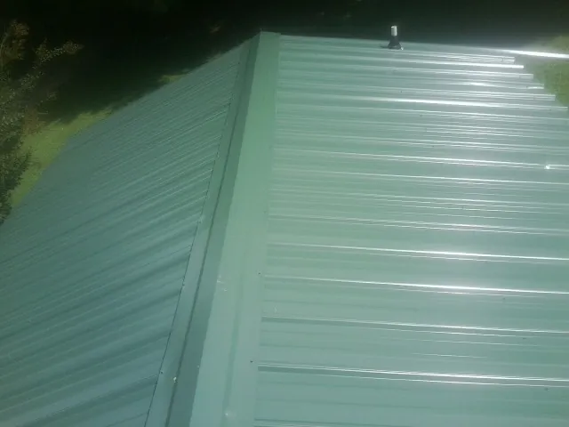 New green metal panels meeting at the ridge of a roof — Flat Roof Repair work by our crew in Wampum