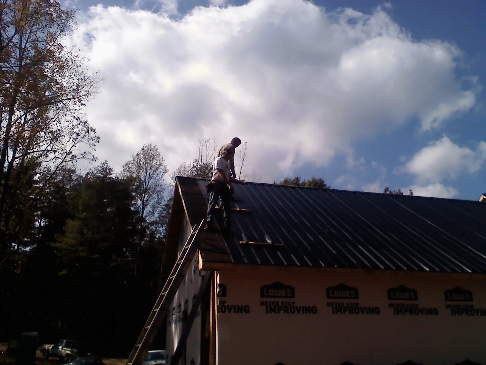 Roofer fastening dark metal panels high against a cloudy sky, from a Roof Inspection job in Wampum