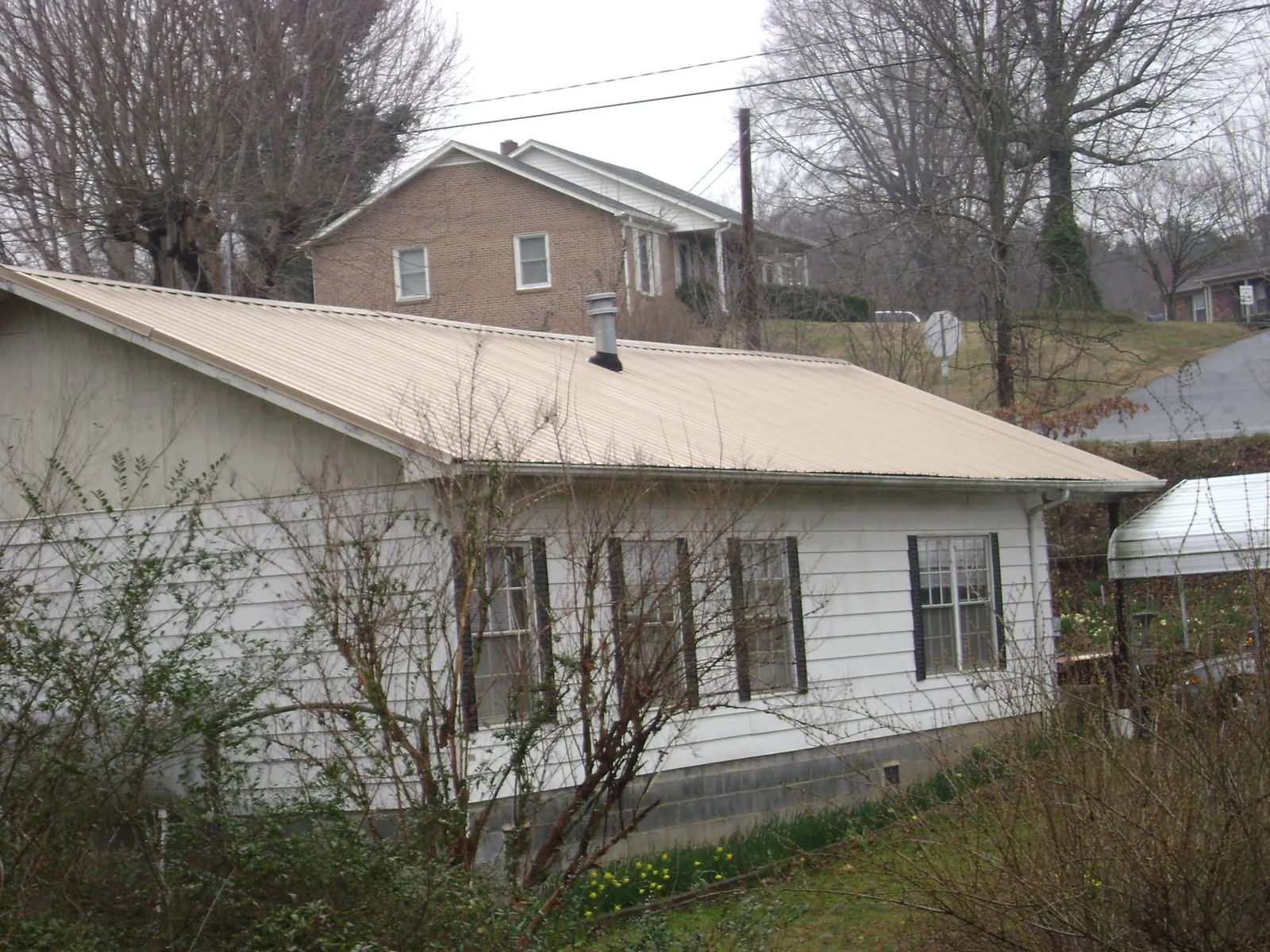 Tan metal roof on a white sided house set into a hillside — Commercial Roofing by Roofing Brothers in Wampum